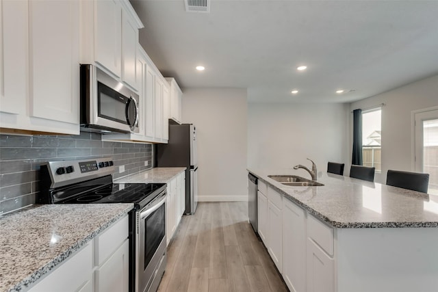 kitchen featuring light stone countertops, white cabinetry, sink, light hardwood / wood-style flooring, and appliances with stainless steel finishes