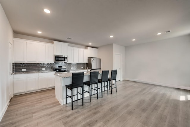 kitchen featuring appliances with stainless steel finishes, light hardwood / wood-style floors, white cabinetry, and a kitchen island with sink