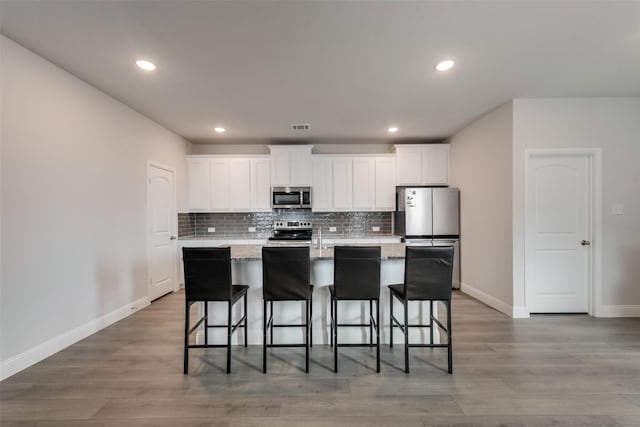 kitchen with white cabinets, a breakfast bar, stainless steel appliances, and a kitchen island with sink