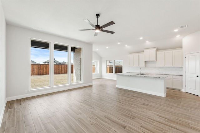 kitchen with white cabinetry, light stone counters, a kitchen island with sink, light hardwood / wood-style floors, and decorative backsplash