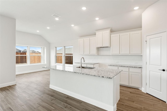 kitchen with white cabinetry, lofted ceiling, sink, and a center island with sink