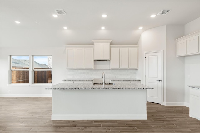 kitchen featuring white cabinetry, sink, light stone countertops, and an island with sink