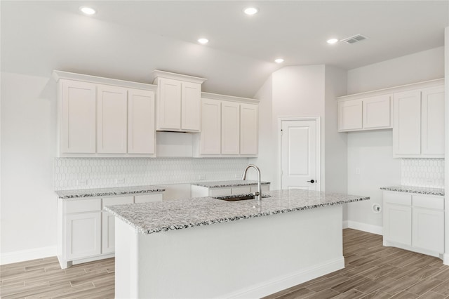 kitchen with light stone countertops, sink, a center island with sink, and white cabinets