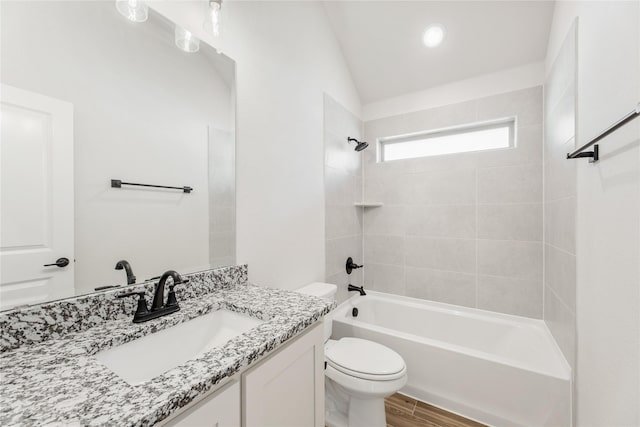 full bathroom with tiled shower / bath, vanity, toilet, and vaulted ceiling