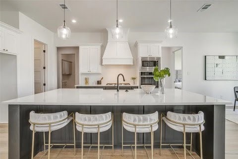 192 Top Flight Dr, Weatherford, TX 76087 - kitchen with premium range hood, white cabinetry, stainless steel microwave, wall oven, and a spacious island
