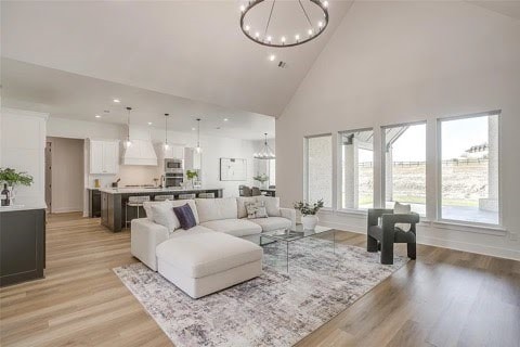 living room with high vaulted ceiling, light wood-type flooring, and a notable chandelier