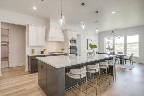 192 Top Flight Dr, Weatherford, TX 76087 - kitchen featuring a large island, premium range hood, light countertops, light wood-style flooring, and stainless steel appliances