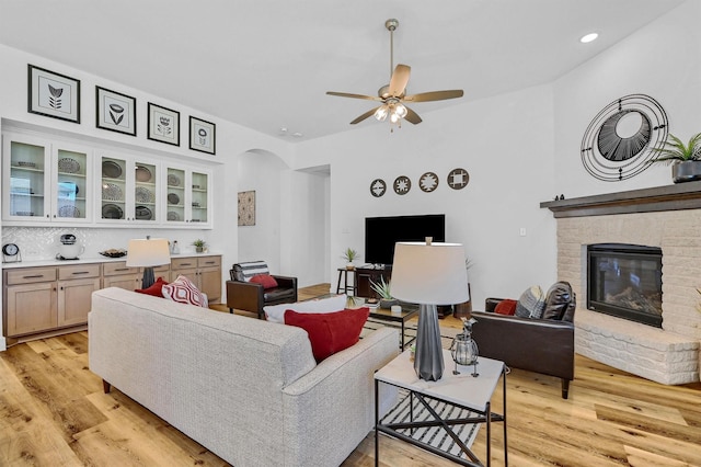 living room with a brick fireplace, ceiling fan, and light wood-type flooring