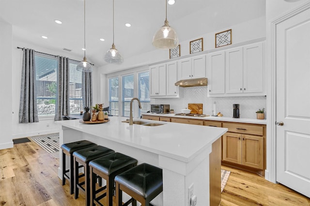 kitchen featuring sink, light hardwood / wood-style floors, decorative light fixtures, a center island with sink, and white cabinets