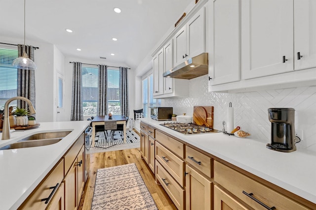 kitchen with sink, hanging light fixtures, appliances with stainless steel finishes, white cabinets, and light wood-type flooring