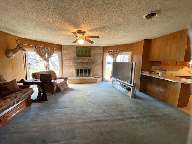 carpeted living room featuring a textured ceiling, wooden walls, ceiling fan, and a healthy amount of sunlight