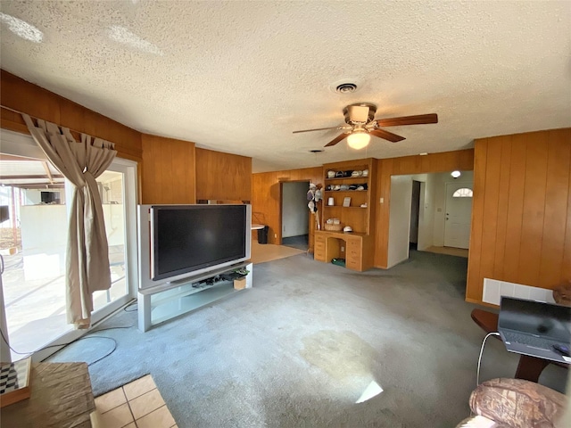 unfurnished living room featuring ceiling fan, light colored carpet, a textured ceiling, and wooden walls