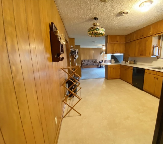 kitchen featuring pendant lighting, dishwasher, wood walls, and a textured ceiling