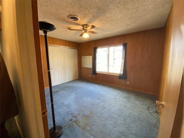 unfurnished bedroom with carpet flooring, a textured ceiling, ceiling fan, a closet, and wood walls