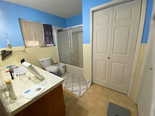 full bathroom with shower / bath combination with glass door, vanity, tile walls, and toilet