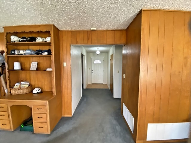 hallway featuring wooden walls, a textured ceiling, and dark colored carpet