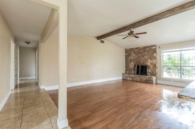 unfurnished living room with hardwood / wood-style floors, ceiling fan, lofted ceiling with beams, and a stone fireplace