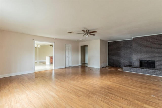 unfurnished living room with a fireplace, ceiling fan with notable chandelier, and light wood-type flooring