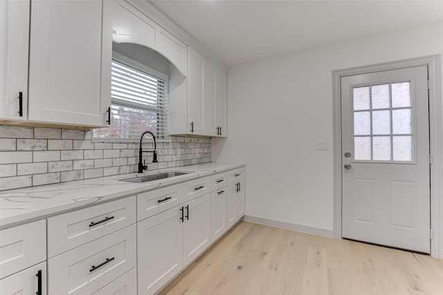 kitchen with light hardwood / wood-style floors, light stone countertops, sink, and white cabinets