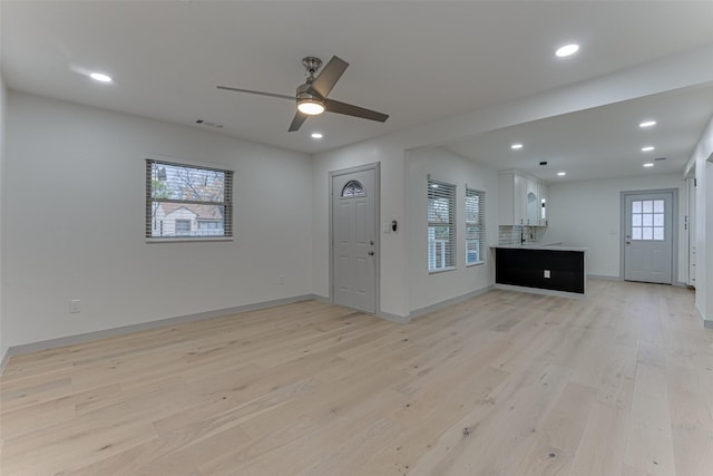 unfurnished living room with ceiling fan, plenty of natural light, sink, and light wood-type flooring