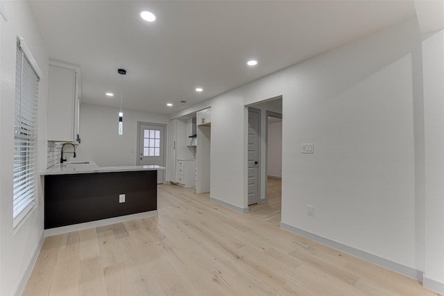 kitchen with white cabinetry, sink, light hardwood / wood-style floors, and kitchen peninsula