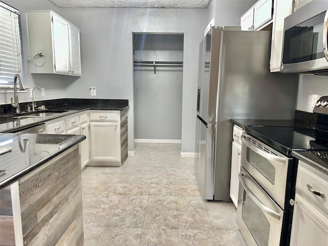 kitchen with stainless steel appliances, sink, white cabinets, and dark stone counters