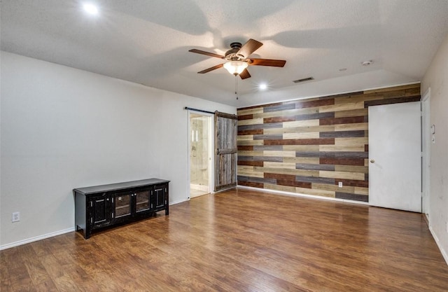 empty room featuring hardwood / wood-style flooring, ceiling fan, a textured ceiling, and wood walls