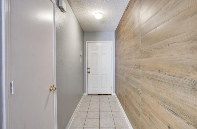 doorway to outside with light tile patterned flooring, wooden walls, and a textured ceiling