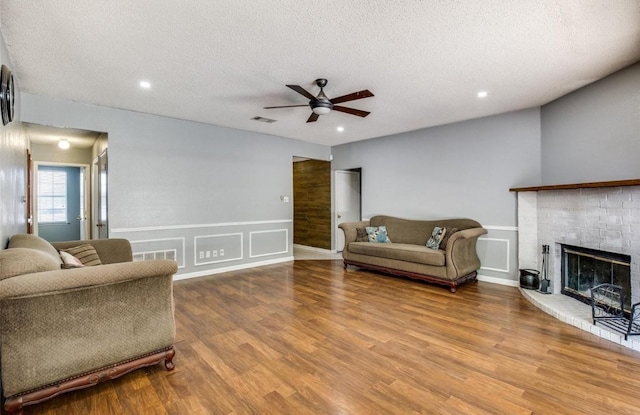 living room with ceiling fan, a textured ceiling, a brick fireplace, and light wood-type flooring