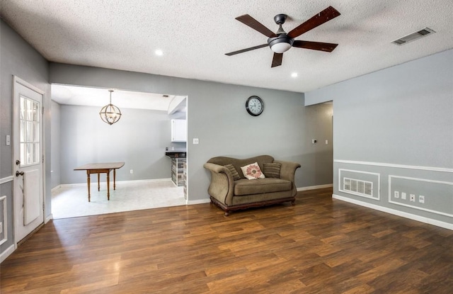 living area featuring ceiling fan with notable chandelier, dark hardwood / wood-style floors, and a textured ceiling