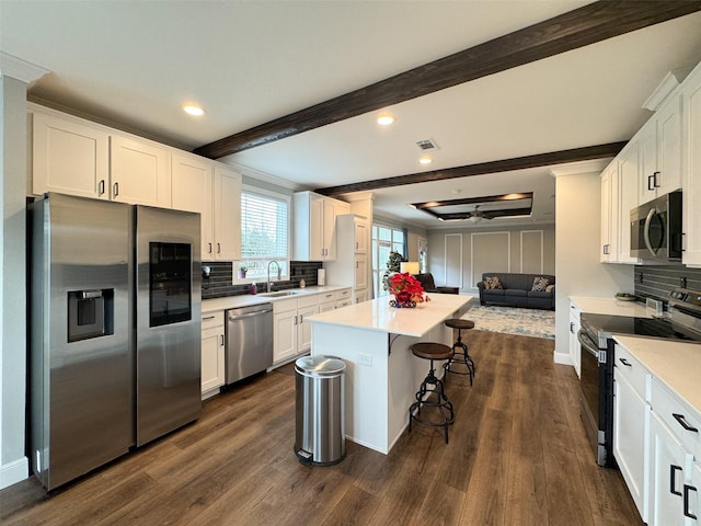 kitchen with dark wood-type flooring, stainless steel appliances, a kitchen island, a breakfast bar area, and white cabinets