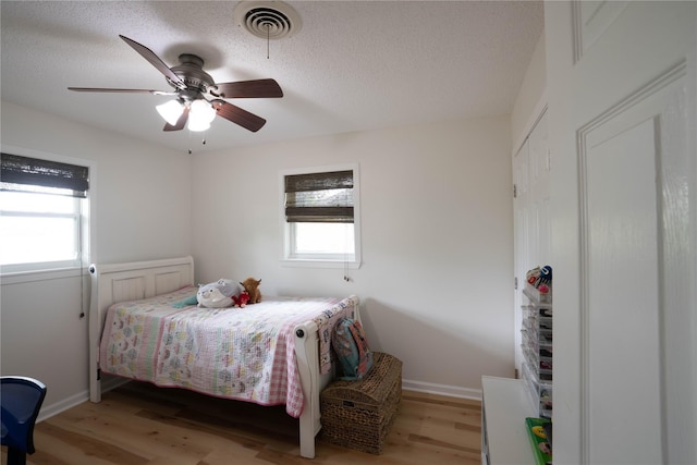 bedroom with a textured ceiling, light hardwood / wood-style flooring, and ceiling fan