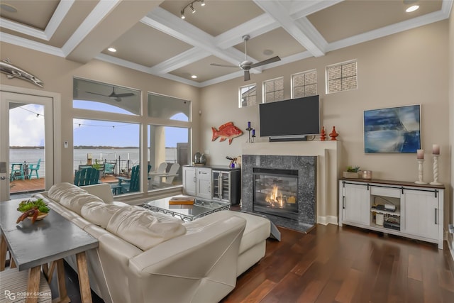 living room with ornamental molding, ceiling fan, dark wood-type flooring, a premium fireplace, and beamed ceiling