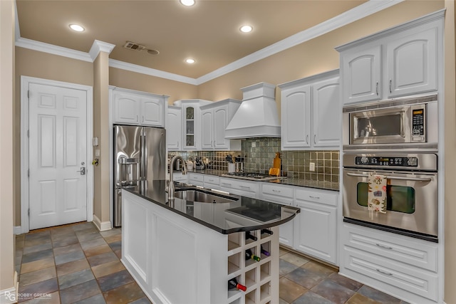 kitchen featuring premium range hood, stainless steel appliances, a kitchen island with sink, sink, and white cabinets