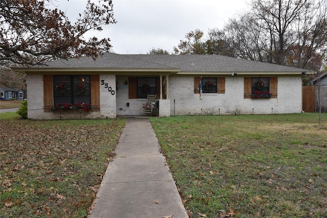 ranch-style home featuring a shingled roof, a front lawn, and brick siding