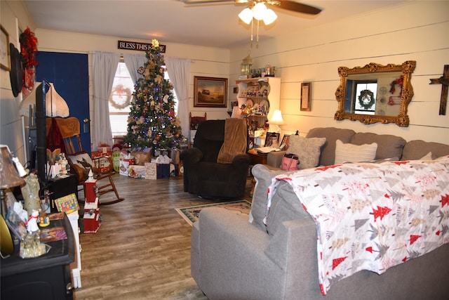 living room with hardwood / wood-style flooring, ceiling fan, and wooden walls