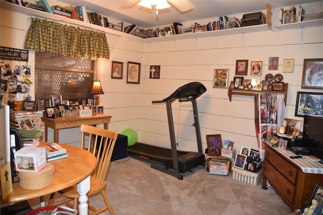 exercise room featuring carpet flooring, ceiling fan, and wooden walls