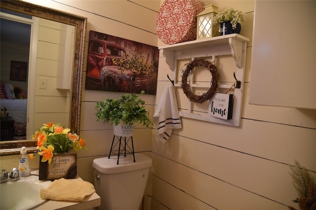 bathroom with toilet, wooden walls, and sink