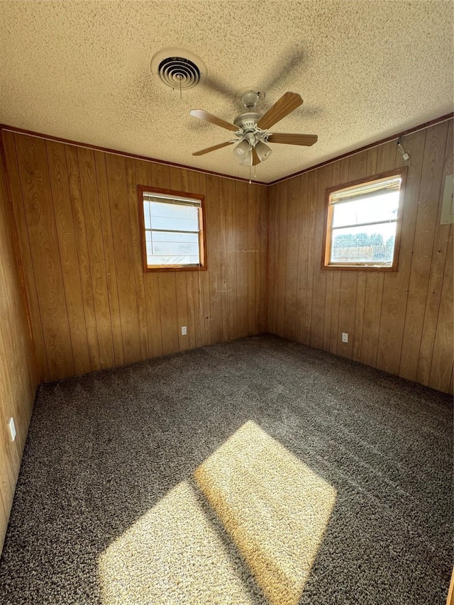 carpeted spare room with wooden walls, ceiling fan, and a textured ceiling