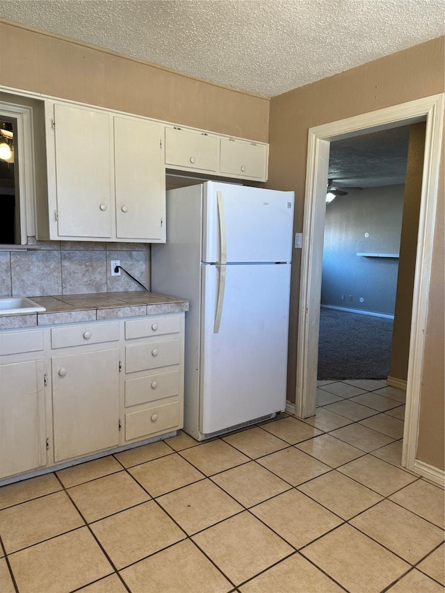 kitchen with white cabinets, light tile patterned floors, backsplash, and white fridge