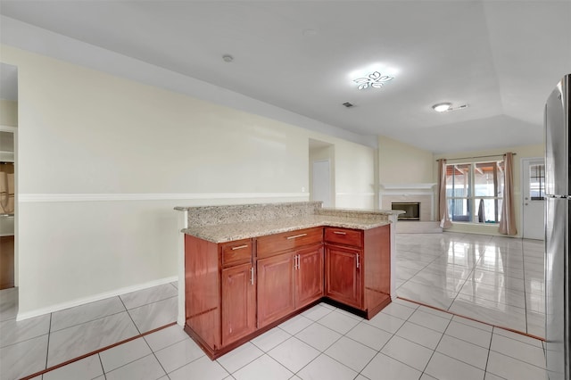 kitchen with stainless steel fridge, light stone countertops, and light tile patterned flooring