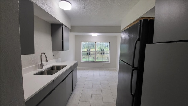 kitchen featuring black refrigerator, sink, light tile patterned floors, and a textured ceiling