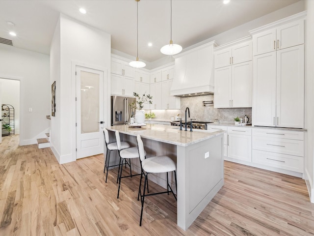 kitchen with white cabinetry, a kitchen island with sink, premium range hood, and high end fridge