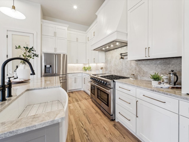 kitchen featuring high quality appliances, decorative light fixtures, custom range hood, decorative backsplash, and white cabinetry