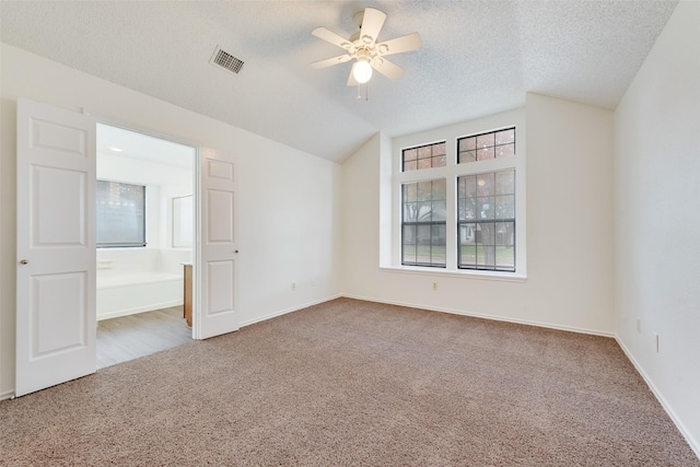 carpeted spare room featuring a textured ceiling, vaulted ceiling, and ceiling fan