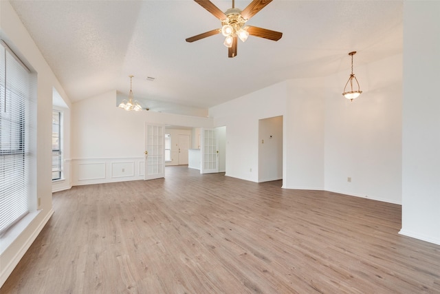 unfurnished living room featuring a textured ceiling, ceiling fan with notable chandelier, lofted ceiling, and light wood-type flooring