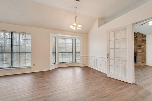 unfurnished room featuring hardwood / wood-style floors, ceiling fan with notable chandelier, a stone fireplace, vaulted ceiling, and a textured ceiling