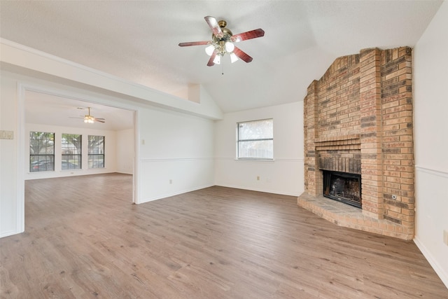 unfurnished living room featuring a brick fireplace, vaulted ceiling, light hardwood / wood-style flooring, and a healthy amount of sunlight