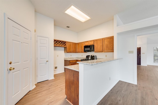 kitchen with light stone countertops, light wood-type flooring, kitchen peninsula, and stainless steel range with gas stovetop