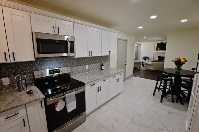 kitchen with light stone countertops, a fireplace, white cabinets, and appliances with stainless steel finishes